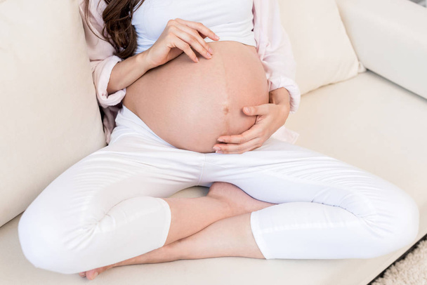 Mulher grávida tocando sua barriga no sofá
 - Foto, Imagem