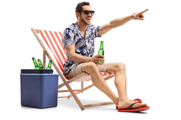 Tourist with a beer sitting in a deck chair and pointing - 写真・画像