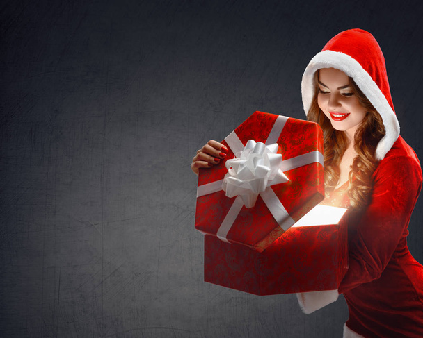 Snow Maiden in red suit smiling holding a gift, opens a gift on - Фото, зображення