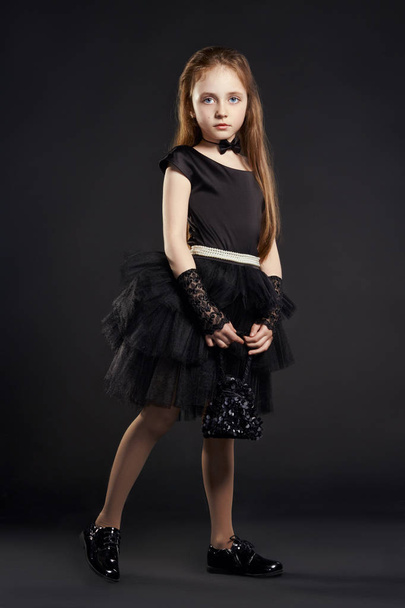 Young girl in a black dress with black bag on a black background. Girl is preparing for Halloween holiday. - Photo, Image