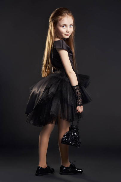 Young girl in a black dress with black bag on a black background. Girl is preparing for Halloween holiday. - Photo, Image