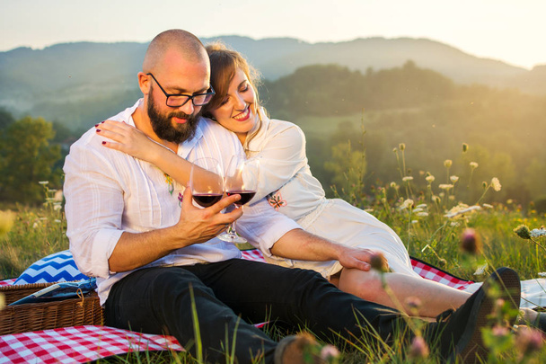 Couple sitting on a picnic blanket with wine glasses - 写真・画像