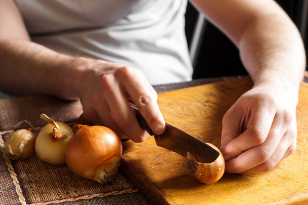 El hombre limpia un cuchillo y corta la cebolla
 - Foto, imagen