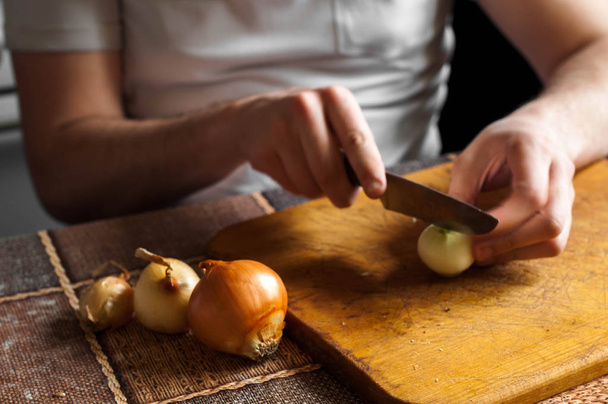 Cortar y cortar una cebolla en una tabla de madera con un cuchillo
 - Foto, Imagen