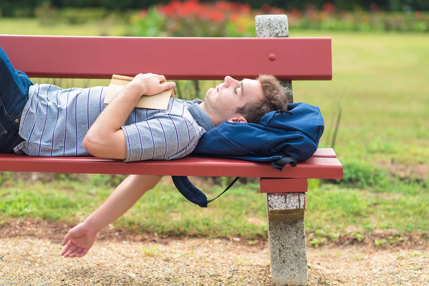 Young man sleeping in the park with a book - Fotó, kép