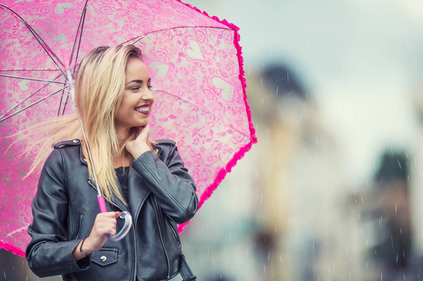 Pembe şemsiye yağmur ve kuvvetli rüzgar ile çekici genç kadın. Sonbahar havalarda şemsiye ile kız. - Fotoğraf, Görsel