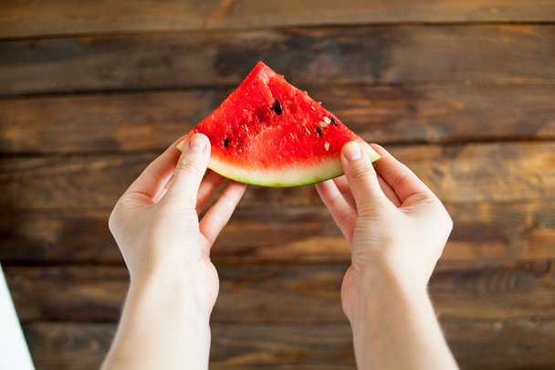 Human hands holding a lump of ripe juicy watermelon in front of him. Wooden background - Photo, Image