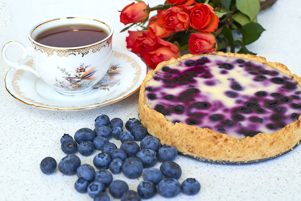 Blueberry pie, kopje thee, heap van bosbessen en rode rozen op een witte achtergrond - close-up - Foto, afbeelding