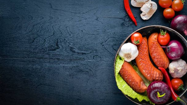 Grilled sausages in a pan with fresh vegetables. Wooden on the black surface. Top view. - Foto, imagen