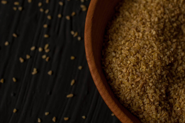 Сухая булгуровая пшеница в коричневой деревянной чаше, изолированная на темном дереве
 - Фото, изображение