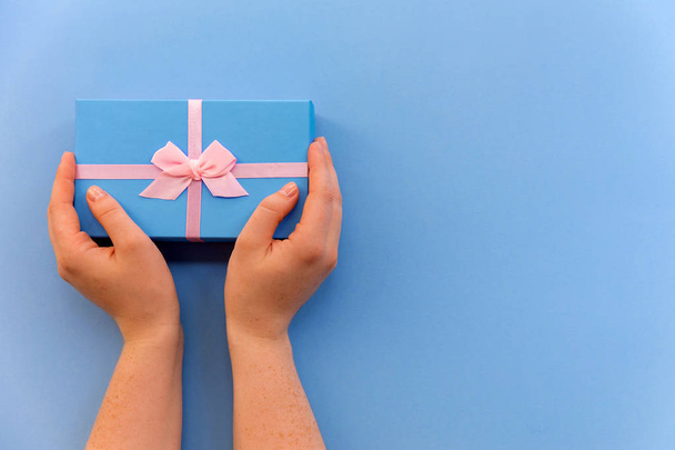 Flatlay holidays giftbox present in woman hands on the pastel blue background for holiday, christmas, birthday party - 写真・画像