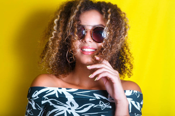 portrait indoors of a young afro american woman in sunglasses. Yellow background. Lifestyle. Casual clothing - Foto, Imagem
