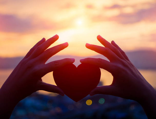 Silhueta mão segurando coração bonito durante o pôr do sol fundo
 - Foto, Imagem