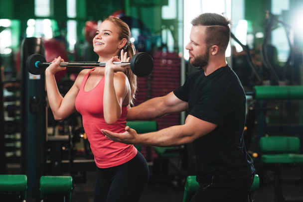 Treinador pessoal ajudando uma jovem mulher a levantar um sino enquanto fazia exercício em um ginásio
 - Foto, Imagem