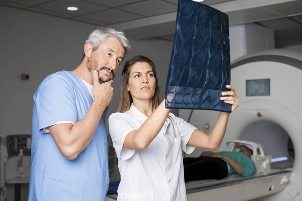 Doctors Examining X-ray With Patient Lying On CT Scan Machine - Photo, image