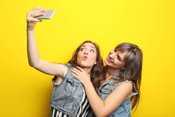 Two young woman making selfie on yellow background - Foto, afbeelding