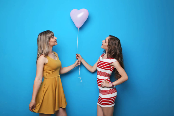 Two young woman with pink heart balloon on blue background - 写真・画像