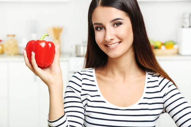 Beautiful young woman with red pepper in the kitchen - Foto, Imagen