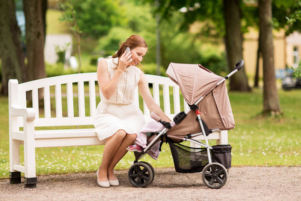 happy mother with smartphone and stroller at park - Zdjęcie, obraz