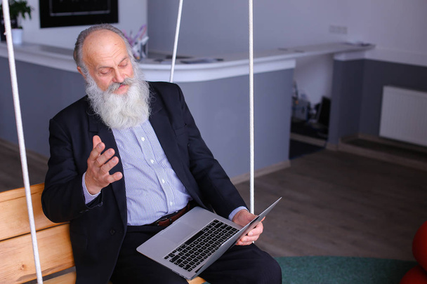 Vecchio uomo in pensione stampe sul computer portatile e colloqui con i colleghi behin
 - Foto, immagini
