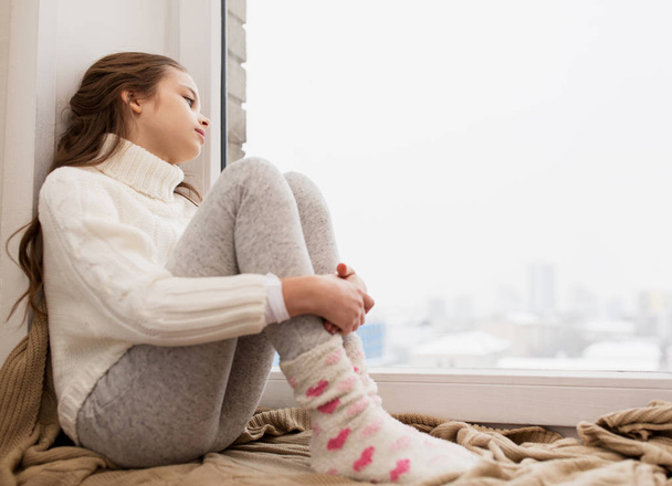 sad girl sitting on sill at home window in winter - Photo, image