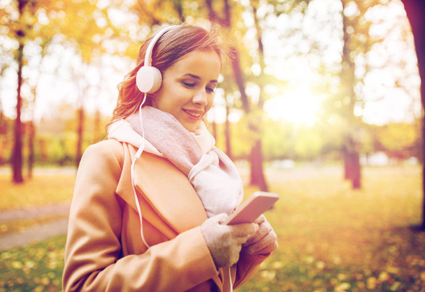 woman with smartphone and earphones in autumn park - Fotografie, Obrázek