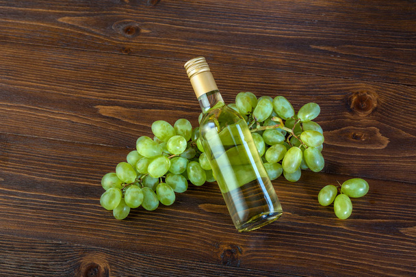 A bottle of white wine with grapes on a wooden background - Photo, image