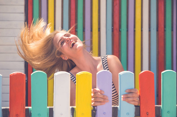 Cheerful female with her hands on colorful fence - Photo, Image