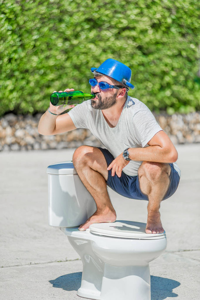 Vousatý muž v brýle rozkročmo na WC, které je instalované - Fotografie, Obrázek