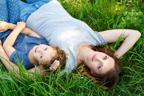 Hermosa joven madre e hija pequeña acostada sobre hierba verde y descansando
 - Foto, Imagen