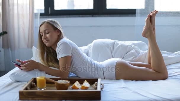 Woman eating breakfast in bed whilst using phone. - Video