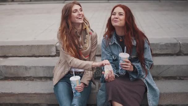 vrolijke vriendinnen zitten op de trappen en eten fastfood - Video