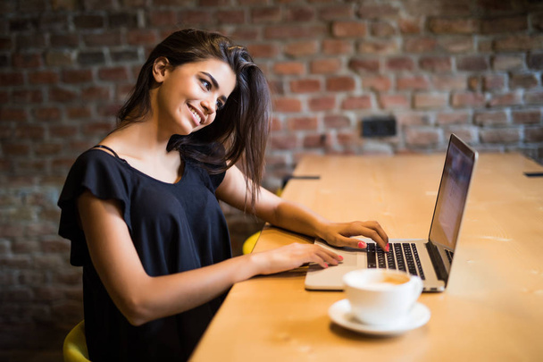 Dizüstü bilgisayar ile kafeteryada oturan ve kahve içmek serbest genç kadın. Kafede dizüstü bilgisayar ile genç kadın. - Fotoğraf, Görsel