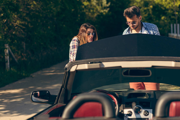 leisure, road trip, travel and people concept - happy friends pushing broken cabriolet car along country road - Zdjęcie, obraz