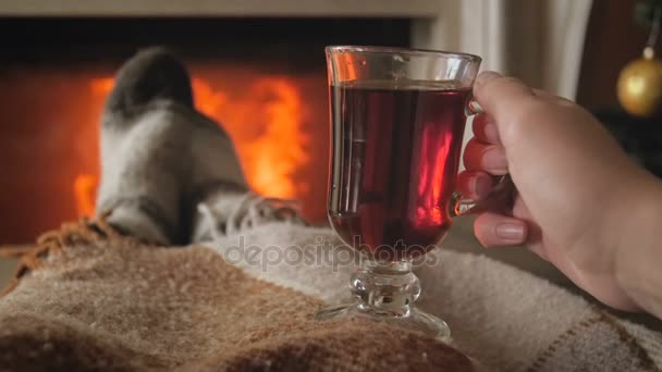 Fechar imagens de câmera lenta de jovem mulher aquecendo pelo fogo na sala de estar e segurando xícara de chá
 - Filmagem, Vídeo