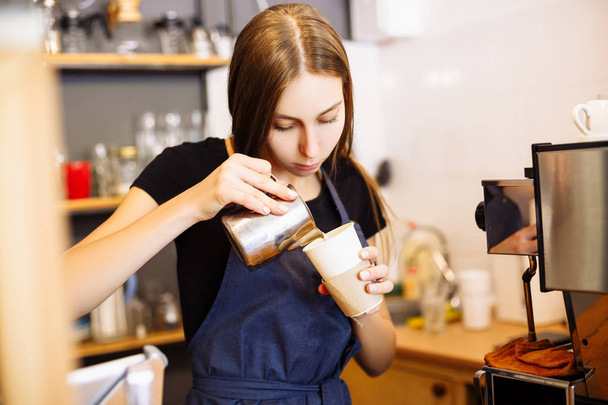 Pretty barista pouring milk into cup of coffee at the coffee shop - Фото, изображение