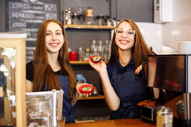 Two happy girls baristas holding donuts in their hands - Фото, зображення