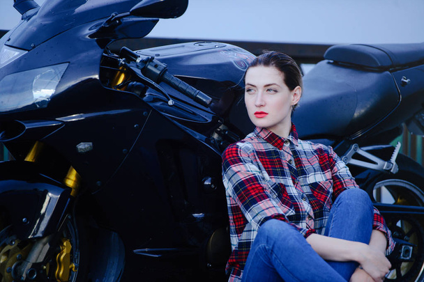 Mujer seria en una camisa sobre un fondo de motocicleta, pelo alisado y lápiz labial rojo
 - Foto, Imagen
