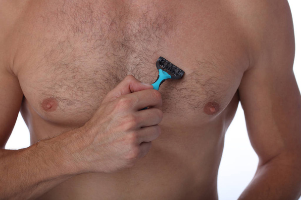 Male depilation. Young attractive muscular man using razor to remove hair from his body - Foto, Bild