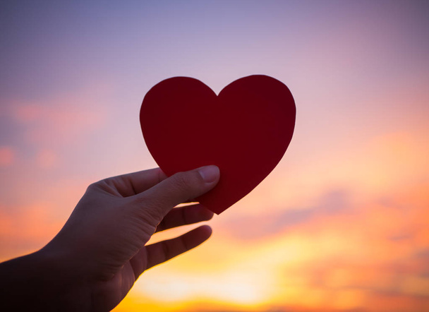 Closeup χέρι κρατά κόκκινη καρδιά κατά τη διάρκεια του ηλιοβασιλέματος φόντο.  - Φωτογραφία, εικόνα