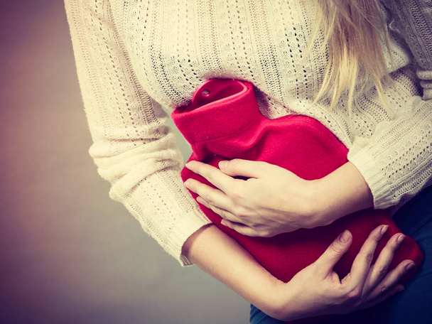 Woman feeling stomach cramps holding hot water bottle - 写真・画像