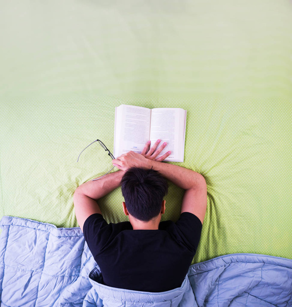Mies yökylässä opiskelemassa kirjaa sängyssä, ylhäältä katsottuna
 - Valokuva, kuva