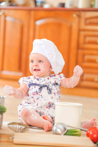 Aranyos liitle lány ül a konyha padló talaj szakács a kalapját - Fotó, kép
