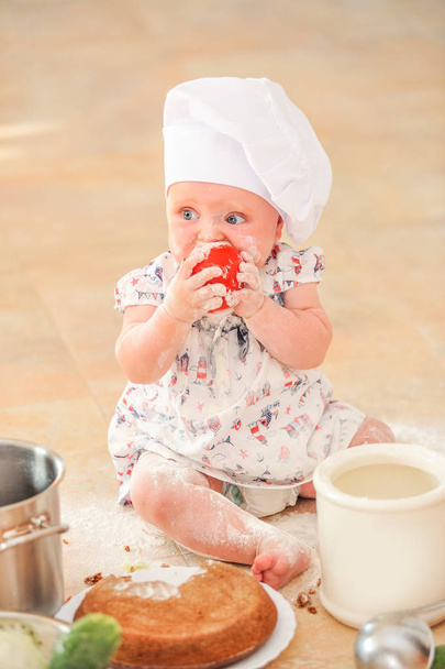 Мила дівчина в капелюсі шеф-кухаря, що сидить на підлозі на кухні
 - Фото, зображення