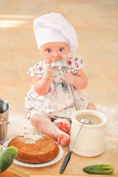 Menina liitle bonito no chapéu do chef sentado no chão da cozinha
 - Foto, Imagem