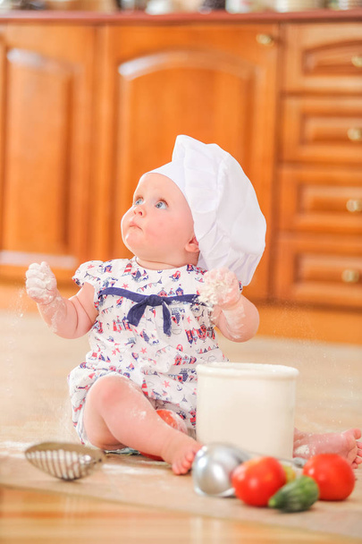 Aranyos liitle lány ül a konyha padló talaj szakács a kalapját - Fotó, kép