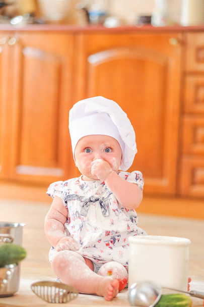 Cute liitle girl in chef's hat sitting on the kitchen floor soil - Фото, изображение