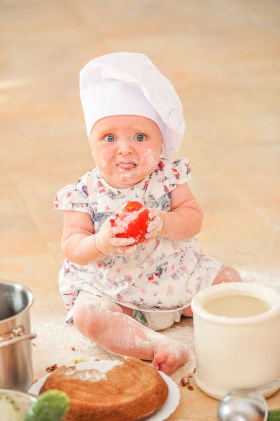 Мила дівчина в капелюсі шеф-кухаря, що сидить на підлозі на кухні
 - Фото, зображення