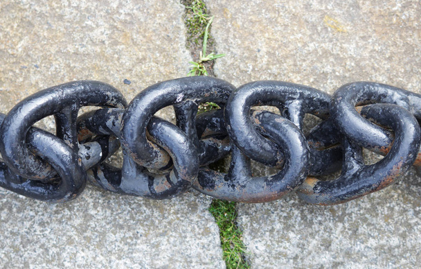 Une chaîne en métal noir avec de grands maillons repose sur des dalles de béton au sol
 - Photo, image