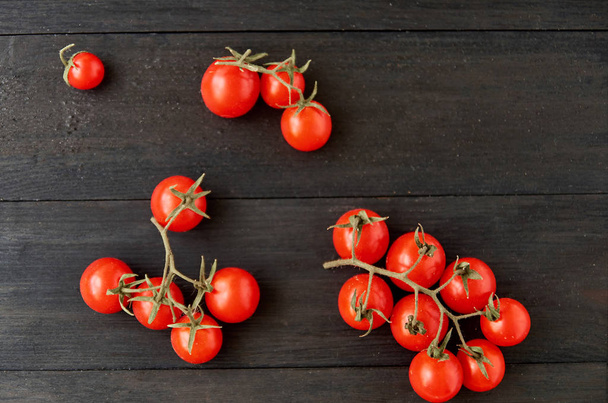 Three branches of red cherry tomatoes isolated on black wooden background - Фото, изображение
